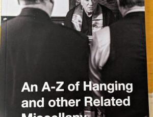 black and white image of the back of a police officer, with prisoner standing in front of a judge. Text to the bottom reads 'An A-Z of Hanging & other Related Miscellany'