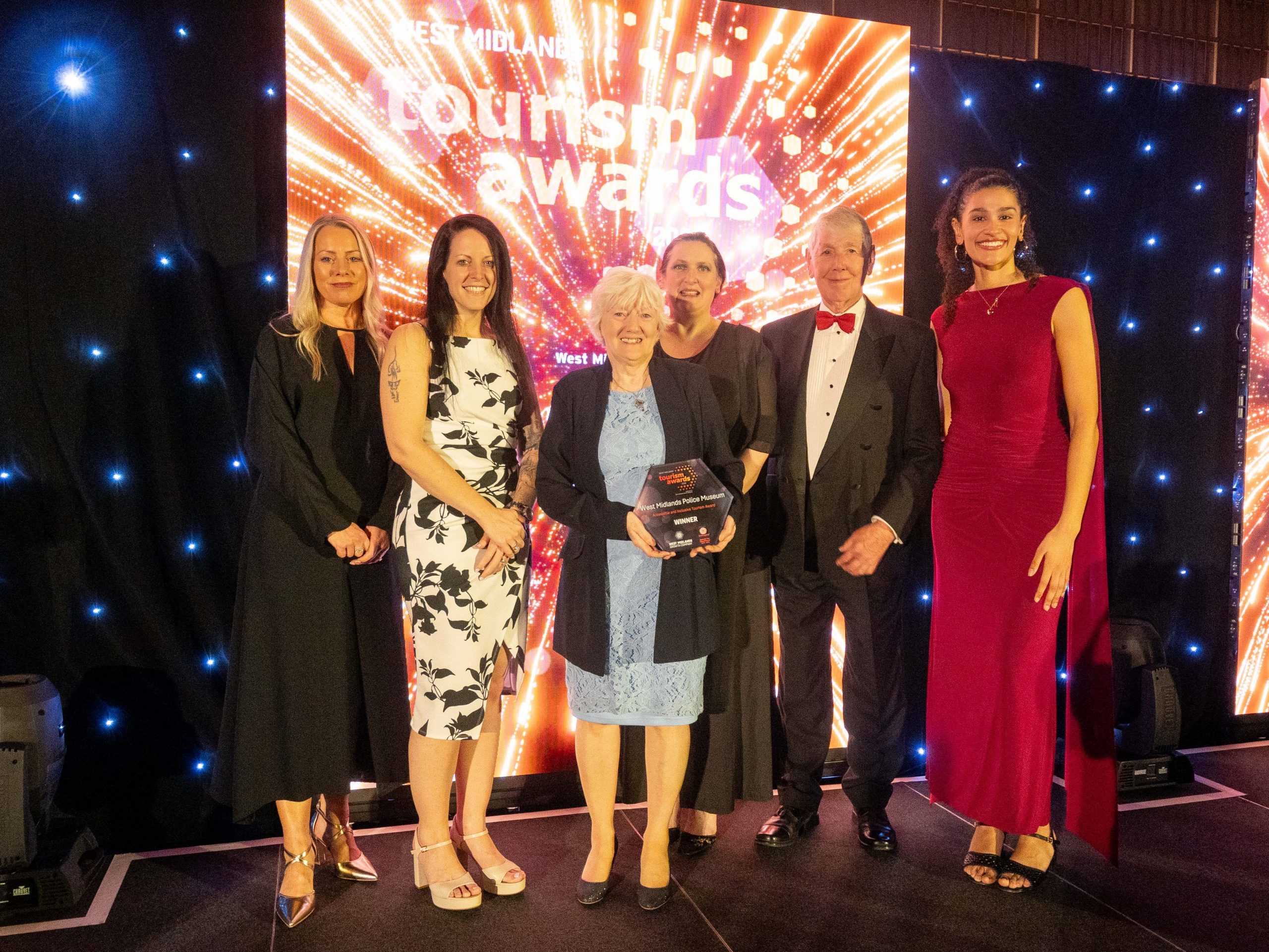 Representatives from the West Midlands Police Museum can be seen holding the Gold Award for Accessibility and Inclusion. They stand upon a stage, in front of a bright background showcasing the awards logo.